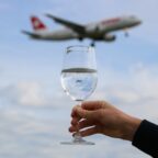 A hand holds a wine glass reflecting the sky, with a blurred airplane flying overhead