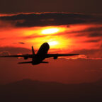 Silhouette of a commercial airplane in flight against a vivid red and orange sunset sky
