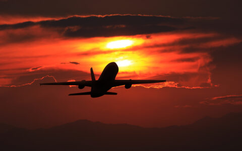 Silhouette of a commercial airplane in flight against a vivid red and orange sunset sky