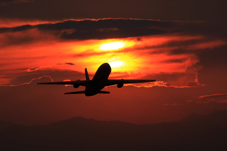 Silhouette of a commercial airplane in flight against a vivid red and orange sunset sky